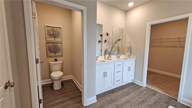 full bath with double vanity, wood finished floors, toilet, baseboards, and a walk in closet