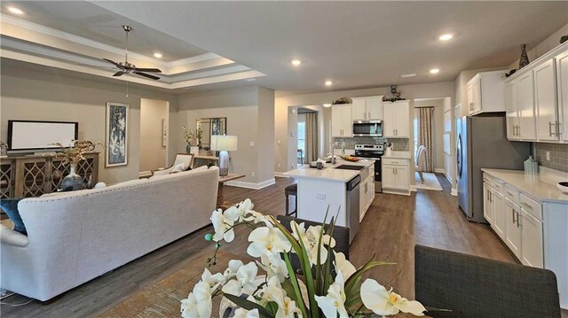 living area featuring crown molding, baseboards, ceiling fan, a tray ceiling, and dark wood finished floors