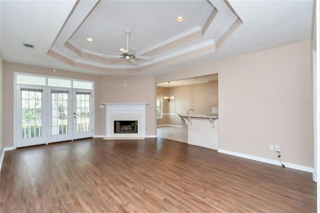 unfurnished living room with hardwood / wood-style floors, ceiling fan with notable chandelier, a tray ceiling, and crown molding