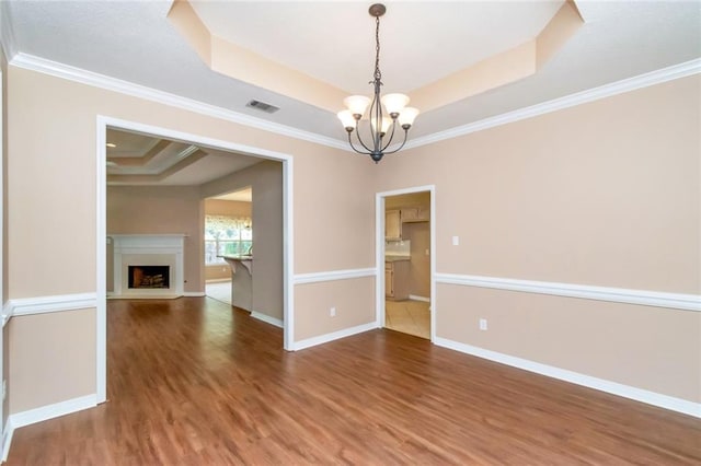 unfurnished room featuring hardwood / wood-style flooring, a raised ceiling, crown molding, and a chandelier