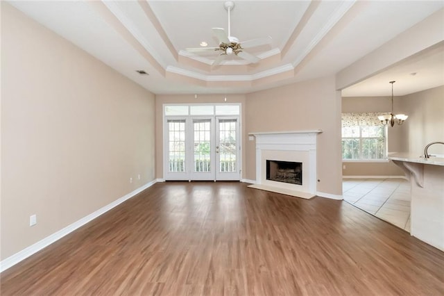 unfurnished living room with ornamental molding, ceiling fan with notable chandelier, a tray ceiling, sink, and wood-type flooring