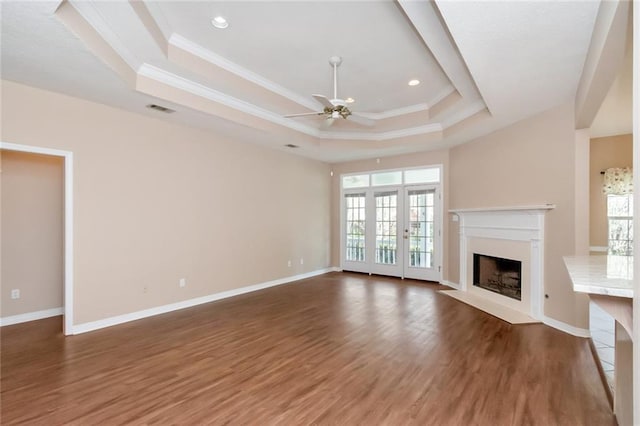 unfurnished living room featuring a raised ceiling, plenty of natural light, ceiling fan, and dark hardwood / wood-style flooring