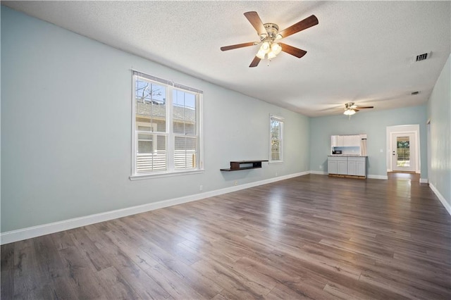 unfurnished living room featuring ceiling fan, dark wood-type flooring, and a textured ceiling