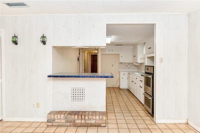 kitchen with white cabinets, tile countertops, stainless steel oven, and visible vents
