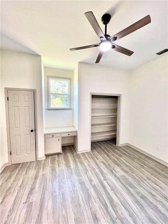 unfurnished bedroom with ceiling fan, built in desk, and light hardwood / wood-style floors