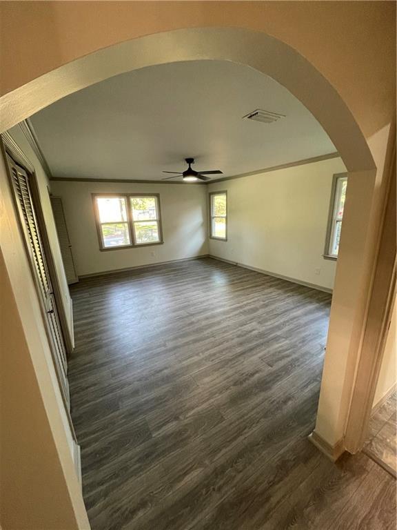 unfurnished living room featuring crown molding, dark wood-type flooring, and ceiling fan