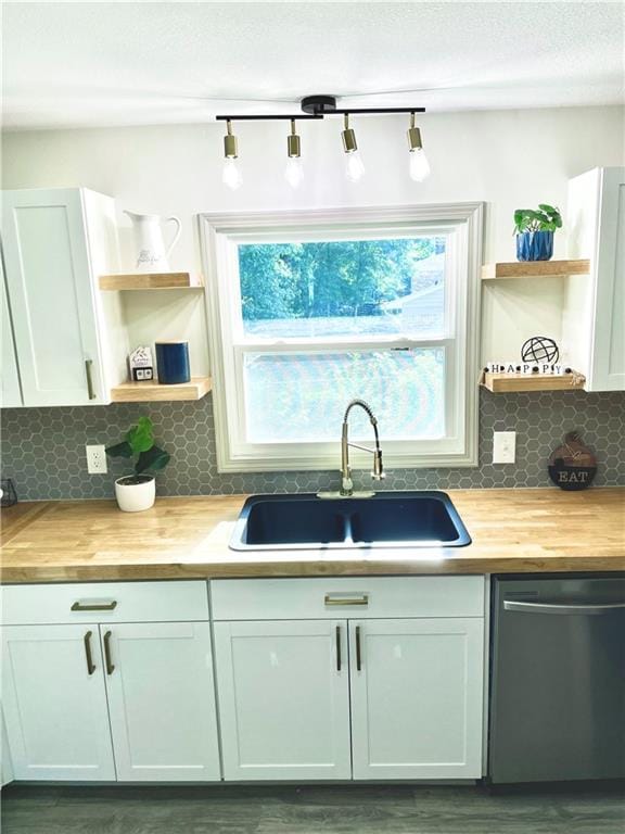 kitchen with dishwashing machine, butcher block countertops, sink, white cabinets, and decorative backsplash