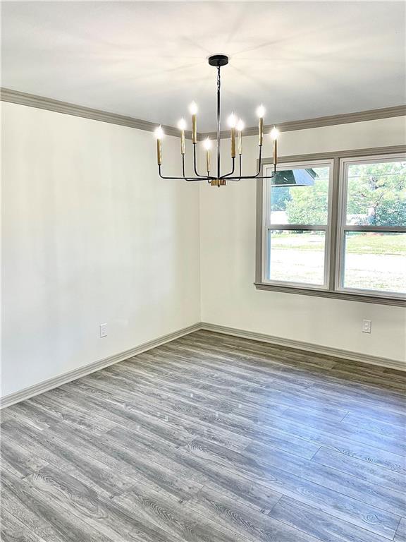 unfurnished dining area with wood-type flooring, ornamental molding, and an inviting chandelier