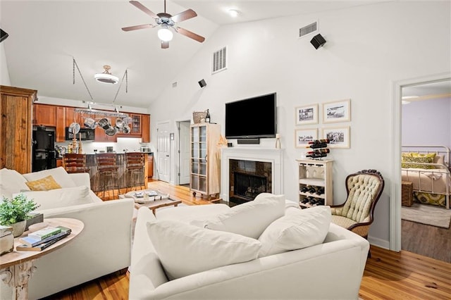 living room with high vaulted ceiling, light wood finished floors, a fireplace, and visible vents