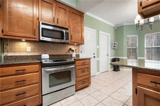 kitchen with light tile patterned floors, appliances with stainless steel finishes, brown cabinetry, and crown molding