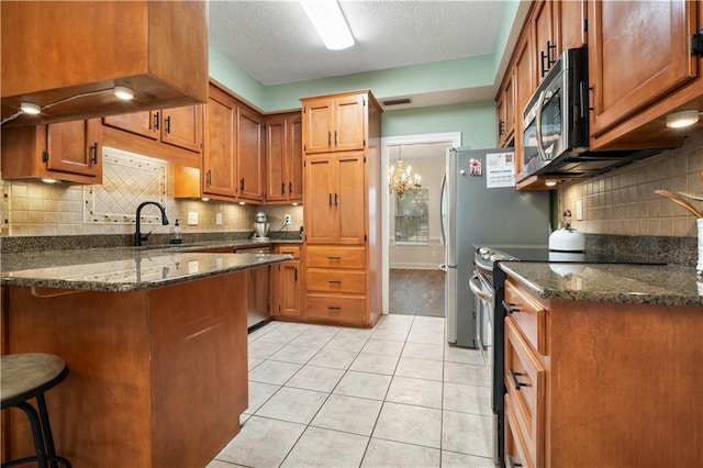 kitchen with light tile patterned floors, brown cabinetry, a peninsula, stainless steel appliances, and a sink