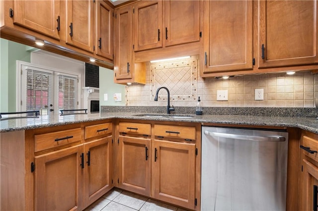 kitchen with dark stone counters, a sink, stainless steel dishwasher, and light tile patterned floors