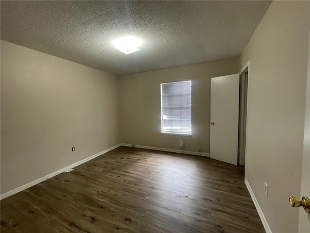 spare room featuring a textured ceiling, baseboards, and dark wood-style flooring