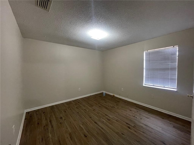 empty room with visible vents, baseboards, dark wood-type flooring, and a textured ceiling