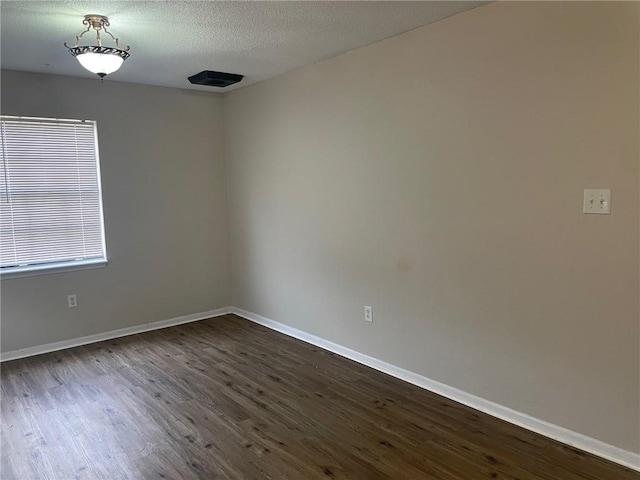 spare room with baseboards, a textured ceiling, and dark wood finished floors