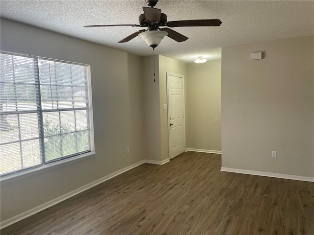 spare room featuring baseboards, dark wood-type flooring, a ceiling fan, and a textured ceiling