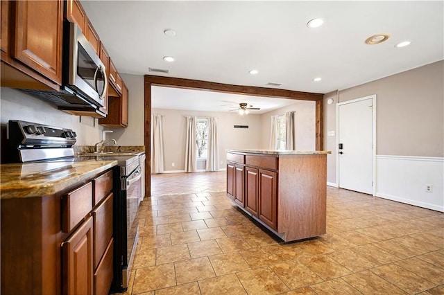 kitchen featuring appliances with stainless steel finishes, light stone counters, ceiling fan, beamed ceiling, and a kitchen island