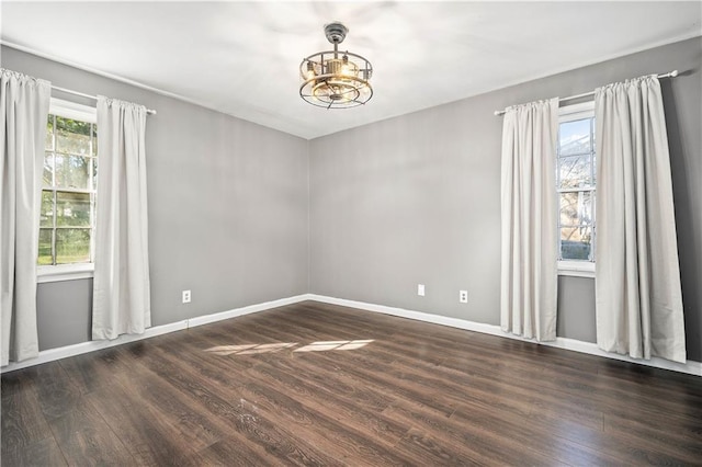 spare room with a chandelier and dark wood-type flooring