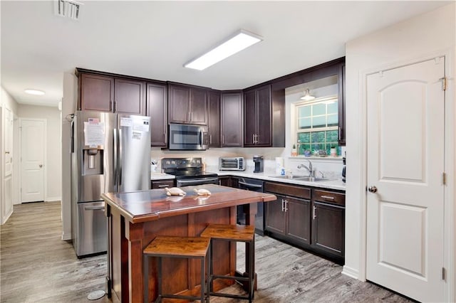 kitchen featuring sink, appliances with stainless steel finishes, dark brown cabinets, a kitchen island, and light wood-type flooring