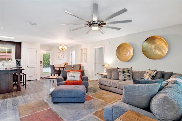 living room with ceiling fan with notable chandelier and light hardwood / wood-style flooring