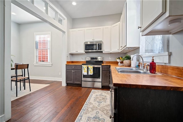 kitchen with butcher block counters, sink, white cabinets, dark hardwood / wood-style flooring, and stainless steel appliances