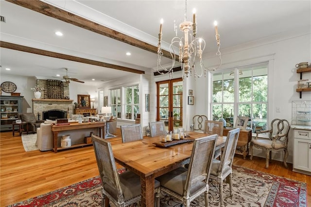 dining space with ceiling fan with notable chandelier, a brick fireplace, a wealth of natural light, and light wood-type flooring