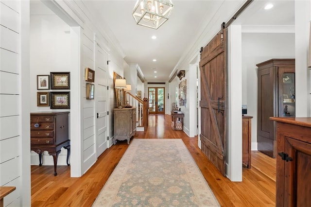 corridor featuring a barn door, ornamental molding, an inviting chandelier, and hardwood / wood-style flooring