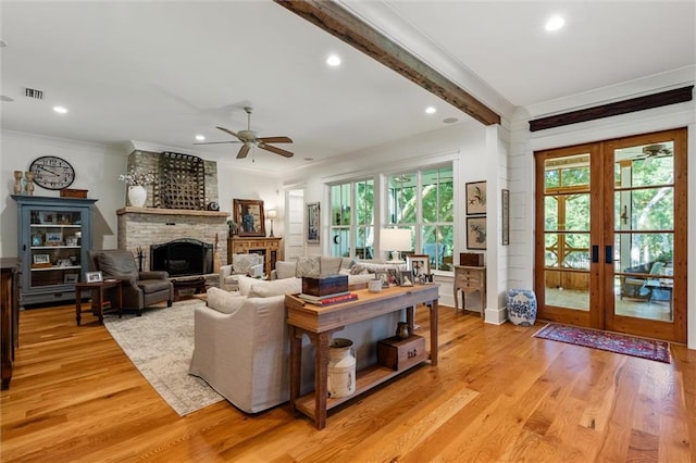 living room with ceiling fan, beam ceiling, french doors, light hardwood / wood-style flooring, and a fireplace