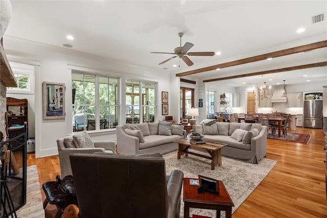 living room featuring ceiling fan with notable chandelier, light hardwood / wood-style floors, and beamed ceiling