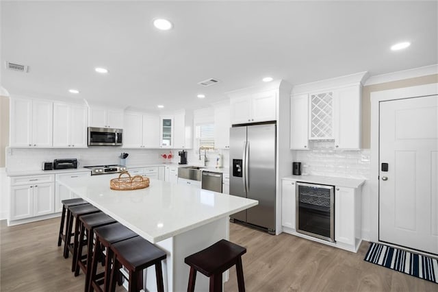 109 Quebec Ct, Dauphin Island, AL 36528 - kitchen featuring appliances with stainless steel finishes, wine cooler, a kitchen breakfast bar, decorative backsplash, and crown molding