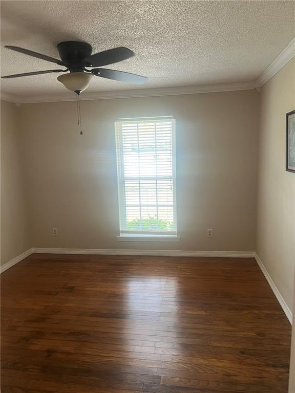 empty room featuring a textured ceiling, wood finished floors, ornamental molding, ceiling fan, and baseboards