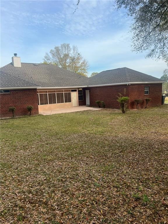 rear view of property featuring a sunroom, a chimney, a lawn, and brick siding