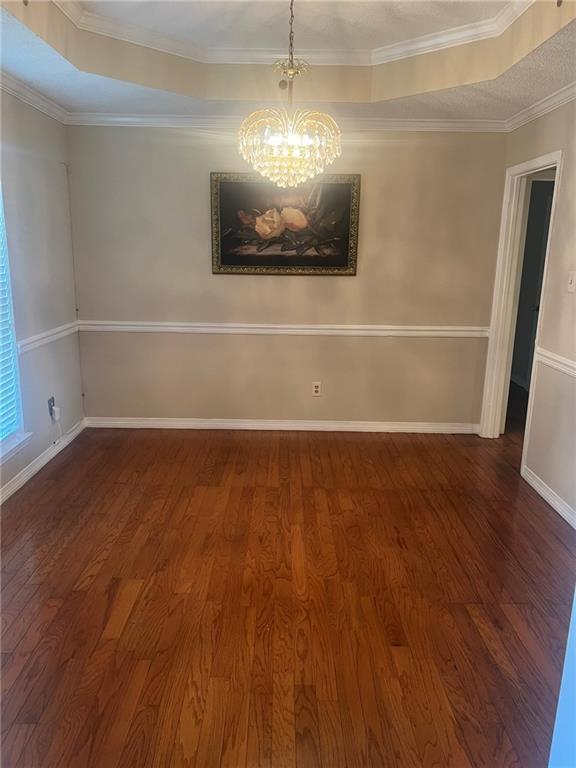 empty room with wood finished floors, a chandelier, baseboards, and crown molding