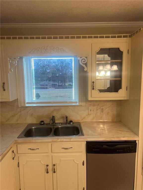 kitchen featuring stainless steel dishwasher, a sink, white cabinetry, decorative backsplash, and crown molding