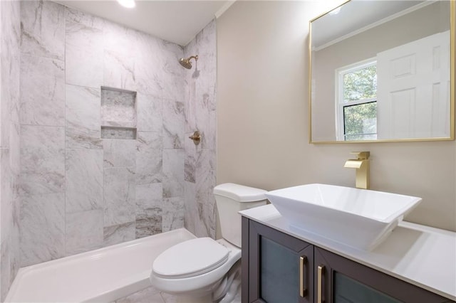 bathroom featuring a tile shower, vanity, toilet, and crown molding