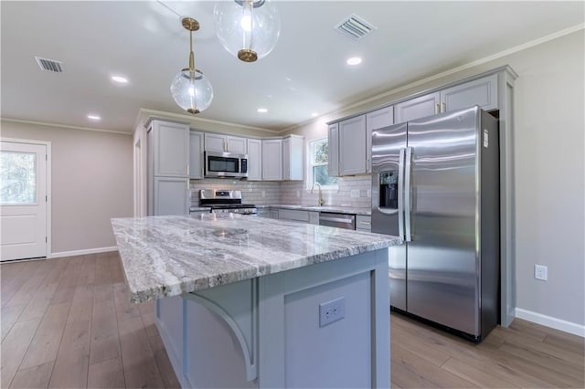 kitchen featuring tasteful backsplash, light stone counters, pendant lighting, a kitchen island, and appliances with stainless steel finishes