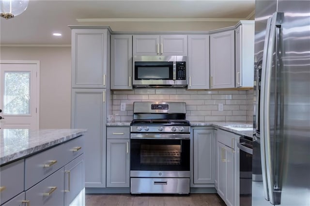 kitchen with gray cabinetry, light stone countertops, crown molding, decorative backsplash, and appliances with stainless steel finishes