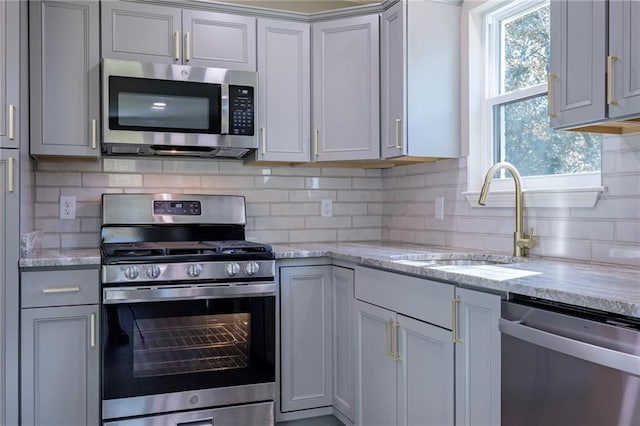 kitchen featuring light stone countertops, appliances with stainless steel finishes, backsplash, and sink