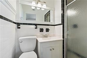full bathroom featuring tile walls, toilet, a stall shower, and vanity