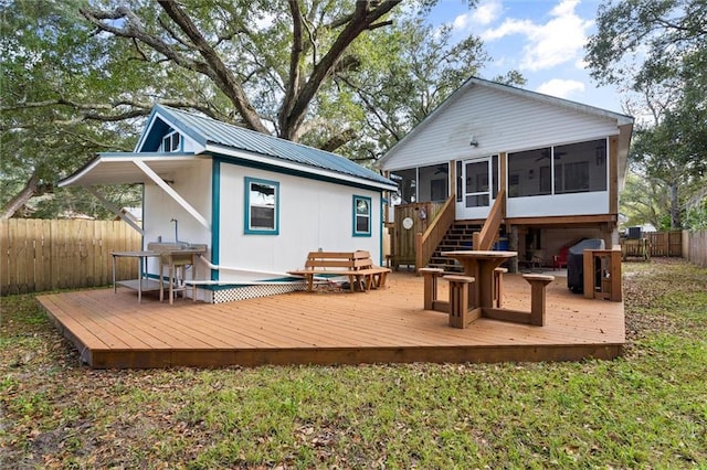 rear view of house featuring a wooden deck, metal roof, a fenced backyard, and a sunroom