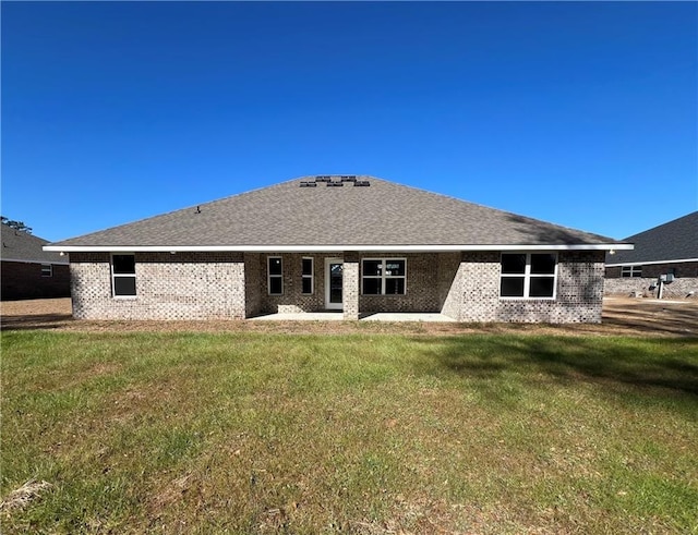 back of house featuring a shingled roof, brick siding, and a yard