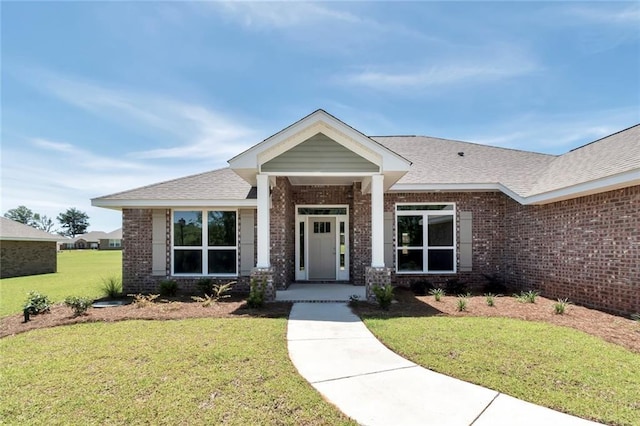 view of front of home featuring brick siding, a front yard, and a shingled roof