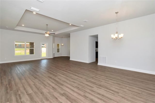 unfurnished living room with ceiling fan with notable chandelier, wood finished floors, visible vents, baseboards, and a tray ceiling