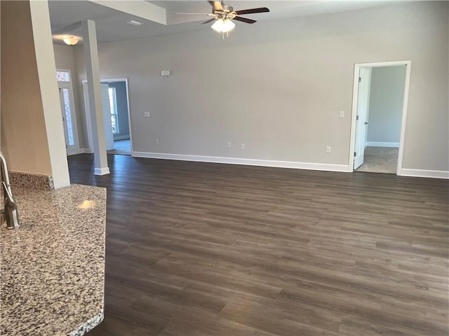 unfurnished living room with a ceiling fan, baseboards, and dark wood-type flooring