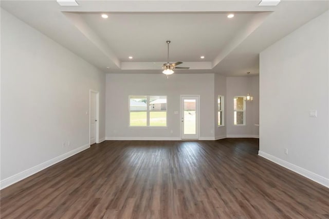 unfurnished living room with dark wood-style floors, recessed lighting, a raised ceiling, and baseboards