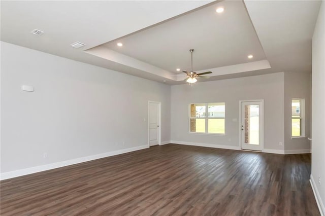 unfurnished living room with dark wood-style floors, a tray ceiling, recessed lighting, and baseboards