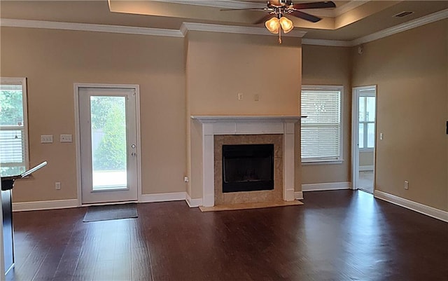 unfurnished living room featuring a tile fireplace, dark wood-type flooring, a tray ceiling, ceiling fan, and crown molding