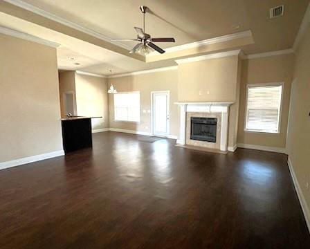 unfurnished living room featuring a tray ceiling, crown molding, ceiling fan with notable chandelier, and dark hardwood / wood-style floors