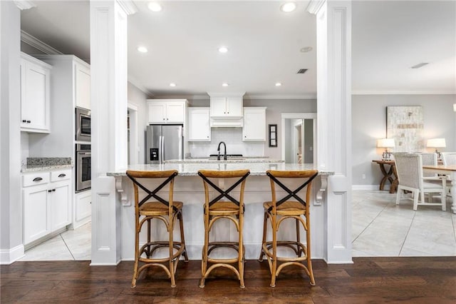 kitchen with light stone countertops, appliances with stainless steel finishes, white cabinetry, and ornate columns