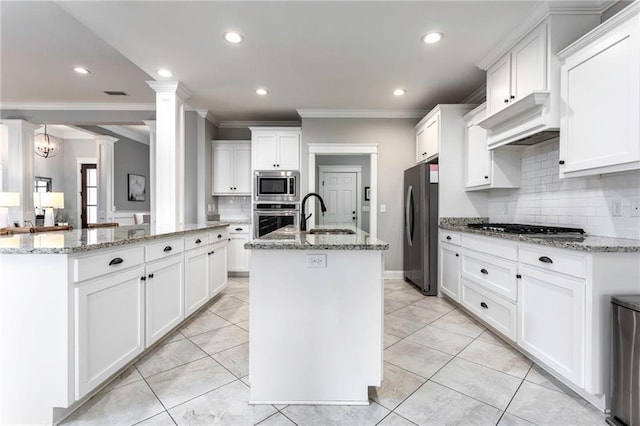 kitchen featuring a center island with sink, appliances with stainless steel finishes, sink, white cabinetry, and decorative columns